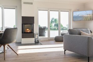 Ein modernes Wohnzimmer mit Kamin, bequemen Sitzmöglichkeiten und Blick durch große Glasfenster.