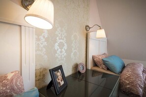 Ein Schlafzimmer mit Glastisch, gerahmtem Foto, gemusterten Kissen und Wandleuchten.