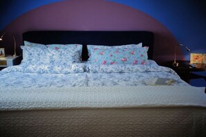 Ein Bett mit floraler Bettwäsche, ein Laptop auf dem Bett und ein Nachttisch mit einer Lampe.