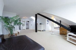 A spacious loft bedroom with a sloped ceiling, a large window, a television, and a potted plant. - Holiday apartment with 2 bedrooms (Fehmarn)