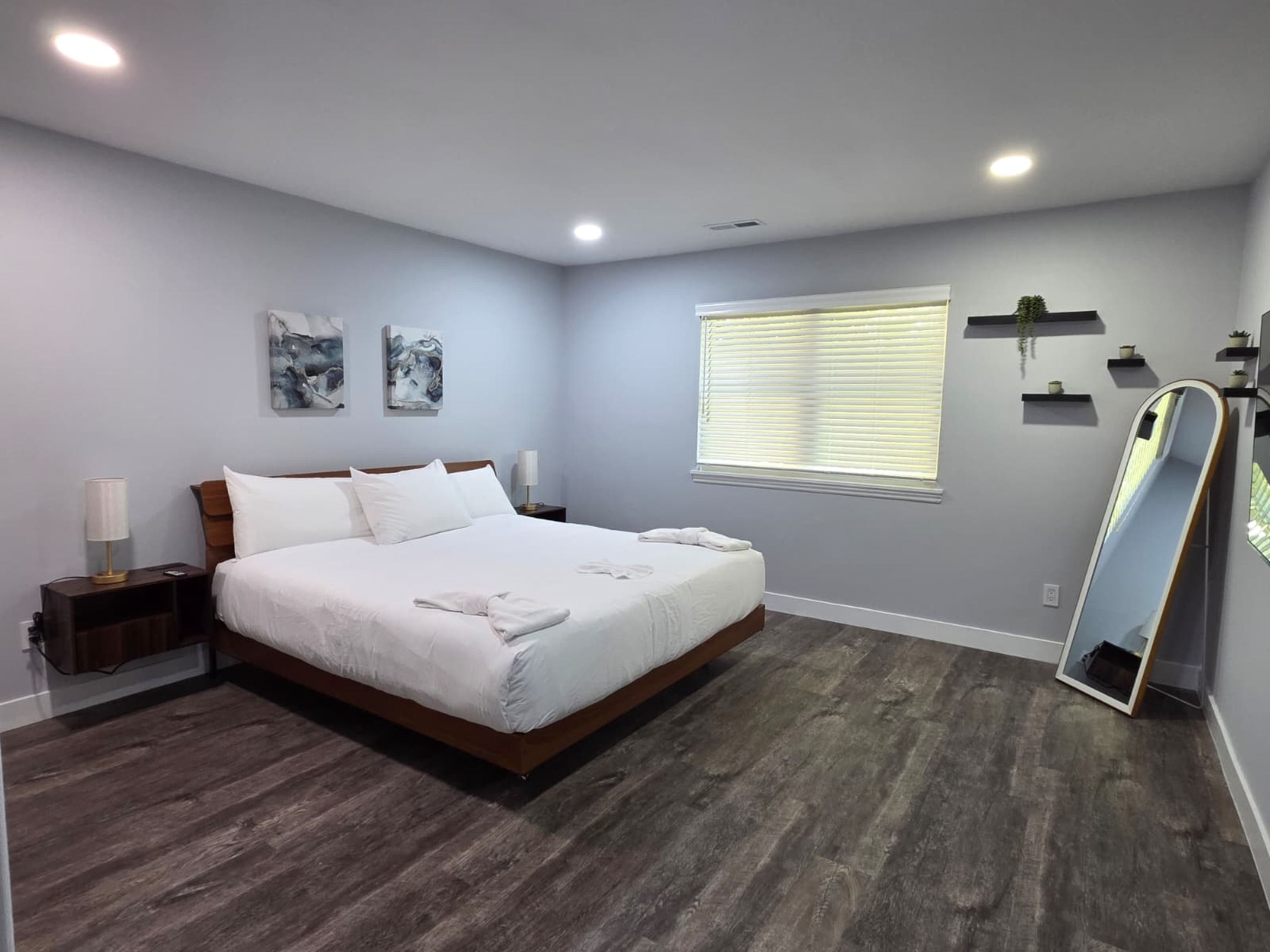 A bedroom with a large bed, bedside tables, a window with blinds, and a mirror.