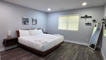 A bedroom with a large bed, bedside tables, a window with blinds, and a mirror.