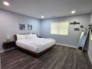 A bedroom with a large bed, bedside tables, a window with blinds, and a mirror. - Pineville Spacious 2BR Home (Pineville)