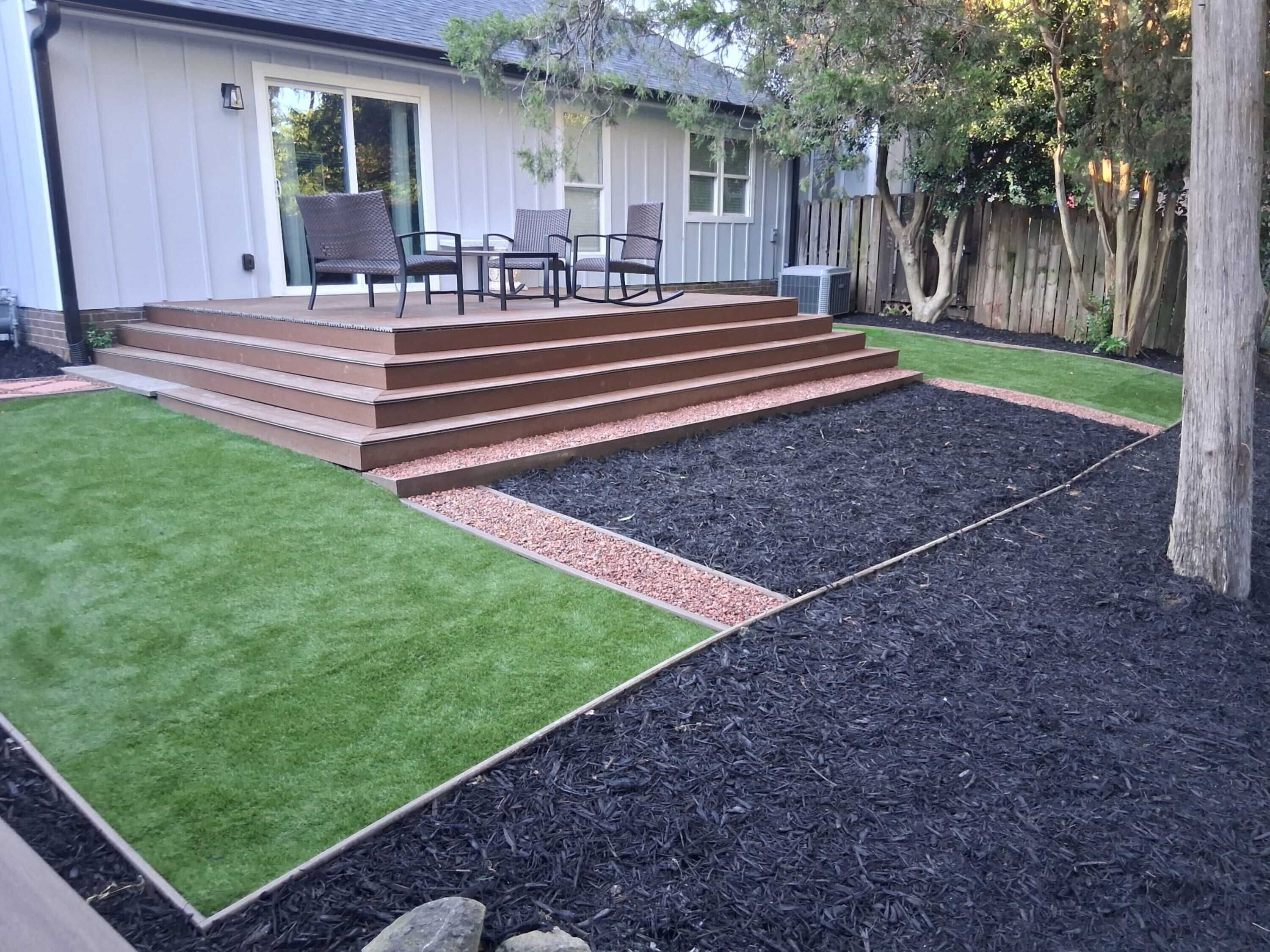 A backyard with a wooden deck, a lawn, and a mulched area.