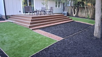 A backyard with a wooden deck, a lawn, and a mulched area.