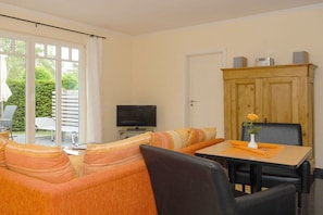 A living room with a sofa, a television, a wooden cabinet, and a dining table with chairs. - Holiday apartment with 1 bedroom (Dierhagen)
