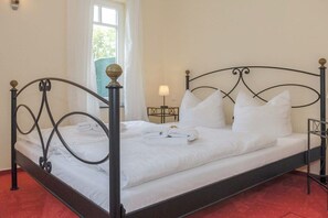 A single bed with a metal frame and white bedding, a bedside table with a lamp, and a window with curtains. - Holiday apartment with 1 bedroom (Dierhagen)