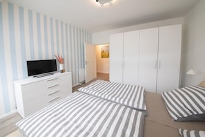Une chambre avec deux lits, une télévision, une armoire et une porte donnant sur une autre pièce.