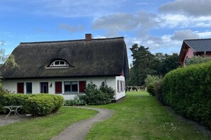 A traditional house with a thatched roof, a paved pathway, and a well-maintained lawn. - At the Old Forester's Lodge (Prerow)