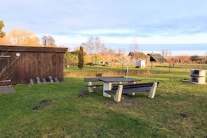 Ein Picknickbereich mit Bänken und einem Tisch, eine Holzhütte und ein kleines Gebäude im Hintergrund.