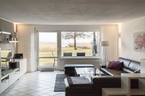 Ein modernes Wohnzimmer mit großem Fenster, einer Couch, einem Couchtisch und einem Fernseher.