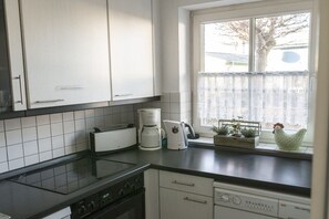 A kitchen with white cabinets, a black countertop, a stove, a coffee maker, and a window with a view of a tree. - Holiday home with 3 bedrooms (Born a. Darß)