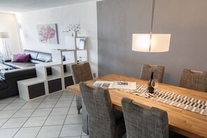 Een moderne woonkamer met een eethoek, met een houten eettafel, grijze beklede stoelen, een witte bank en een grijze accentmuur.