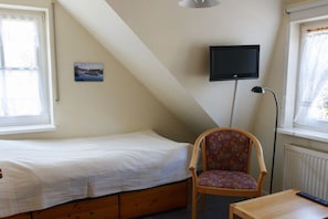 A small, single-bed room with a sloped ceiling, a mounted television, a chair, and a table. - Holiday home with 2 bedrooms (Born a. Darß)