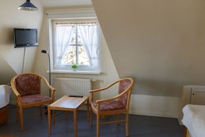A room with two wooden chairs, a small table, a bed, a television mounted on the wall, and a window with curtains. - Holiday home with 2 bedrooms (Born a. Darß)