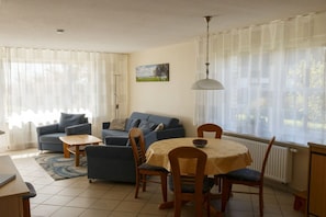 A living room with a sofa, a dining table with chairs, and a painting on the wall. - Holiday home with 2 bedrooms (Born a. Darß)