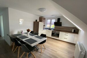 A modern kitchen with a dining area, featuring a table with chairs, a built-in oven, and a window with blinds. - Holiday apartment with 3 bedrooms (Oldenburg in Holstein)