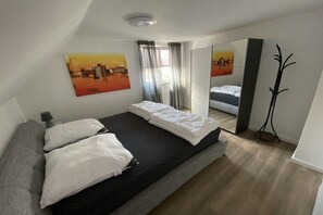A bedroom with a bed, a bedside table, a mirror, and a window with curtains. - Holiday apartment with 3 bedrooms (Oldenburg in Holstein)