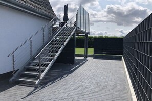 Eine Treppe führt zu einem Gebäudeeingang, an einer Seite befindet sich ein Metallgeländer und ein schwarzer Zaun.