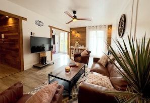A living room with a flat-screen TV, a ceiling fan, a dining area with a table and chairs, and a large plant. - Little Nashville - 3 min from Disney - 35 min from Paris (Chessy)