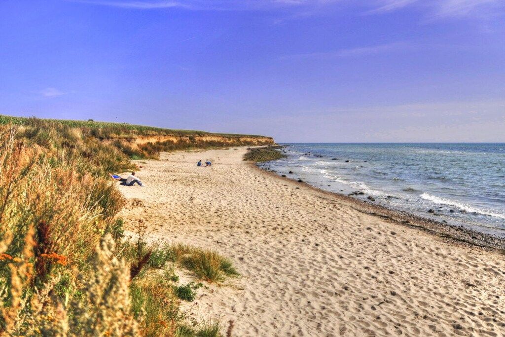 Ein Sandstrand mit einer grasbewachsenen Klippe und dem Meer.