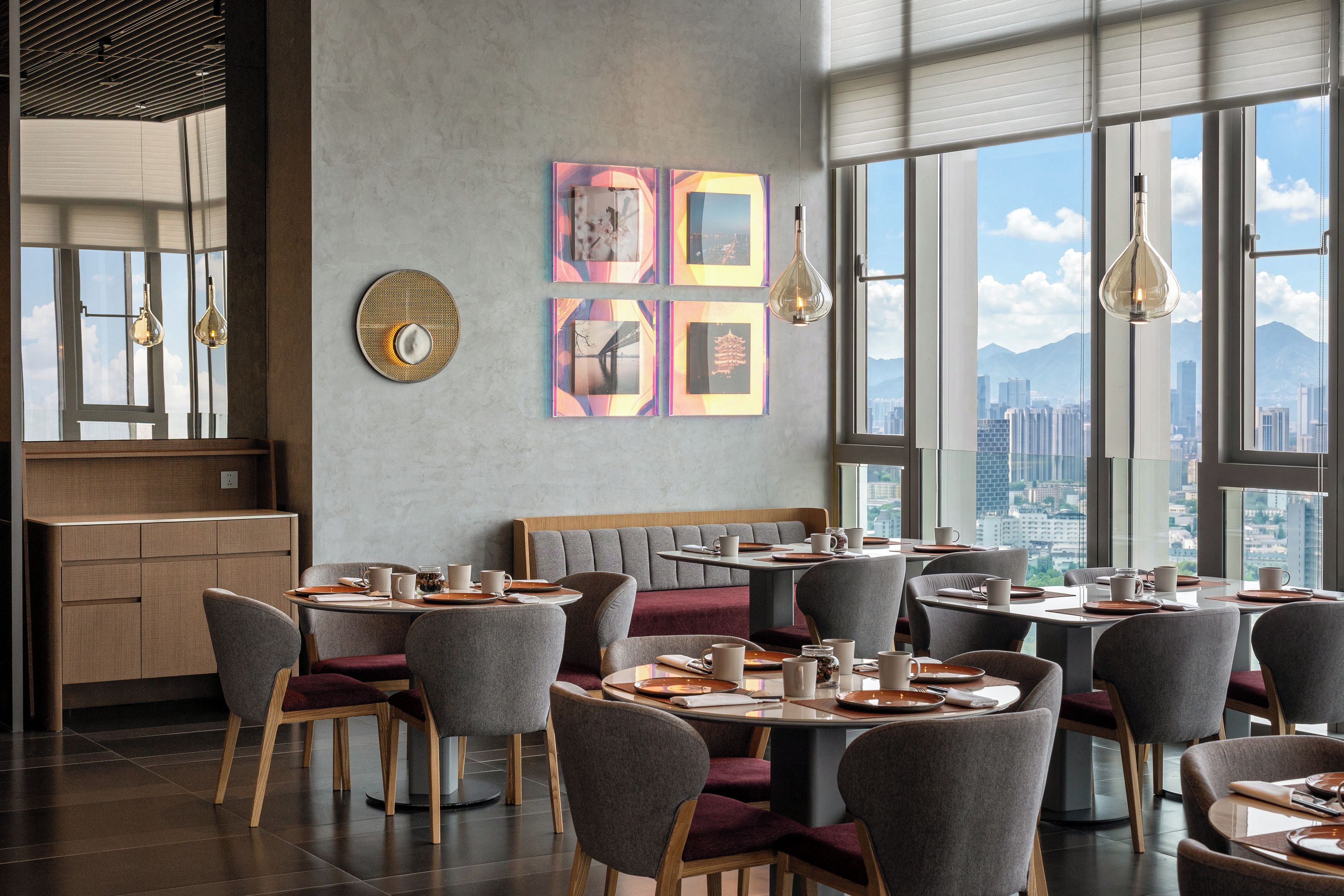 Un comedor moderno con mesas redondas, sillas tapizadas de gris y vistas a la ciudad a través de amplios ventanales.