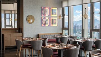 Un comedor moderno con mesas redondas, sillas tapizadas de gris y vistas a la ciudad a través de amplios ventanales.