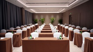 A conference room with rows of tables, chairs, and potted plants.