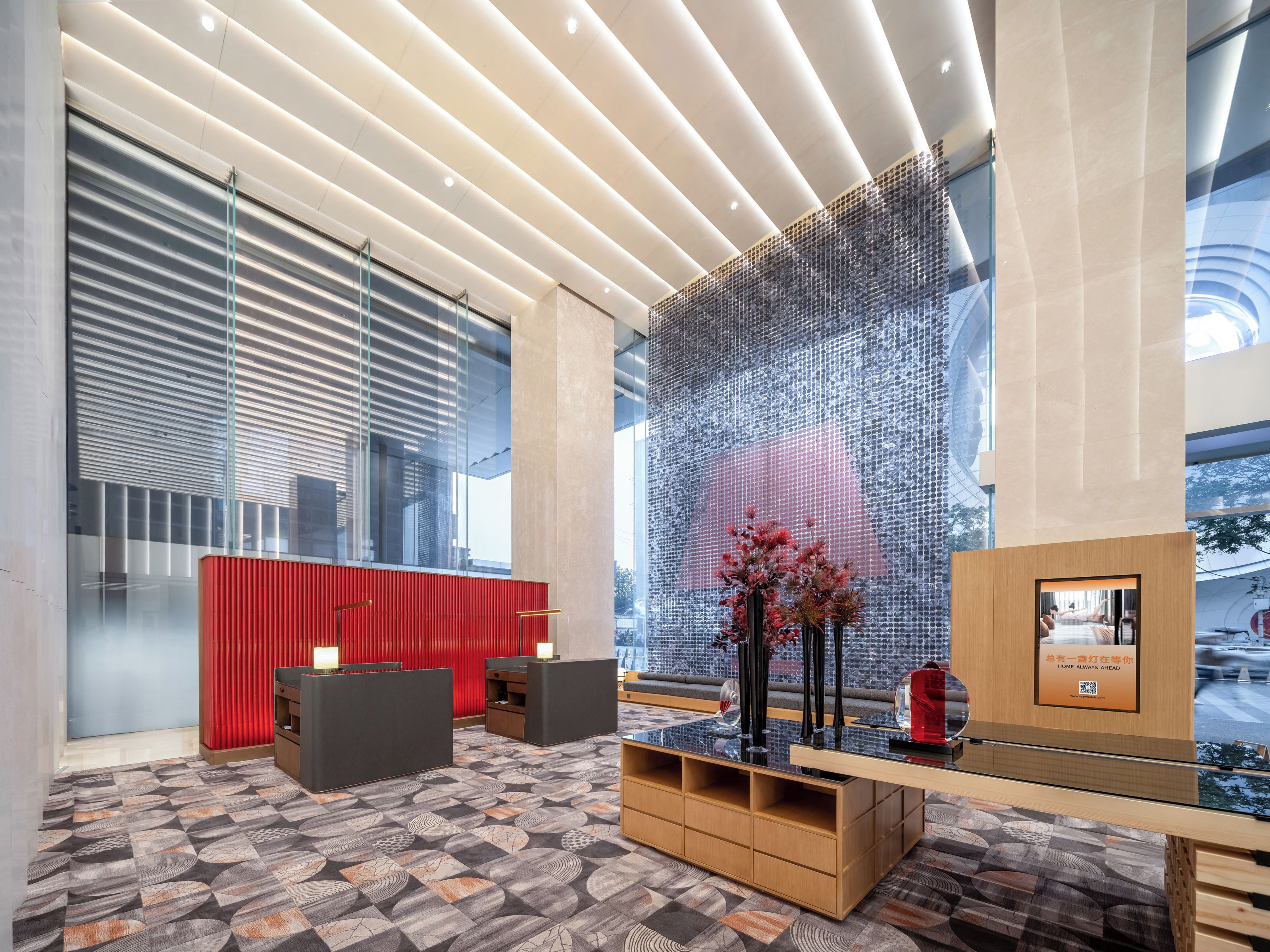 A modern reception area with a patterned carpet, a red reception desk, and a large glass wall with a decorative screen.