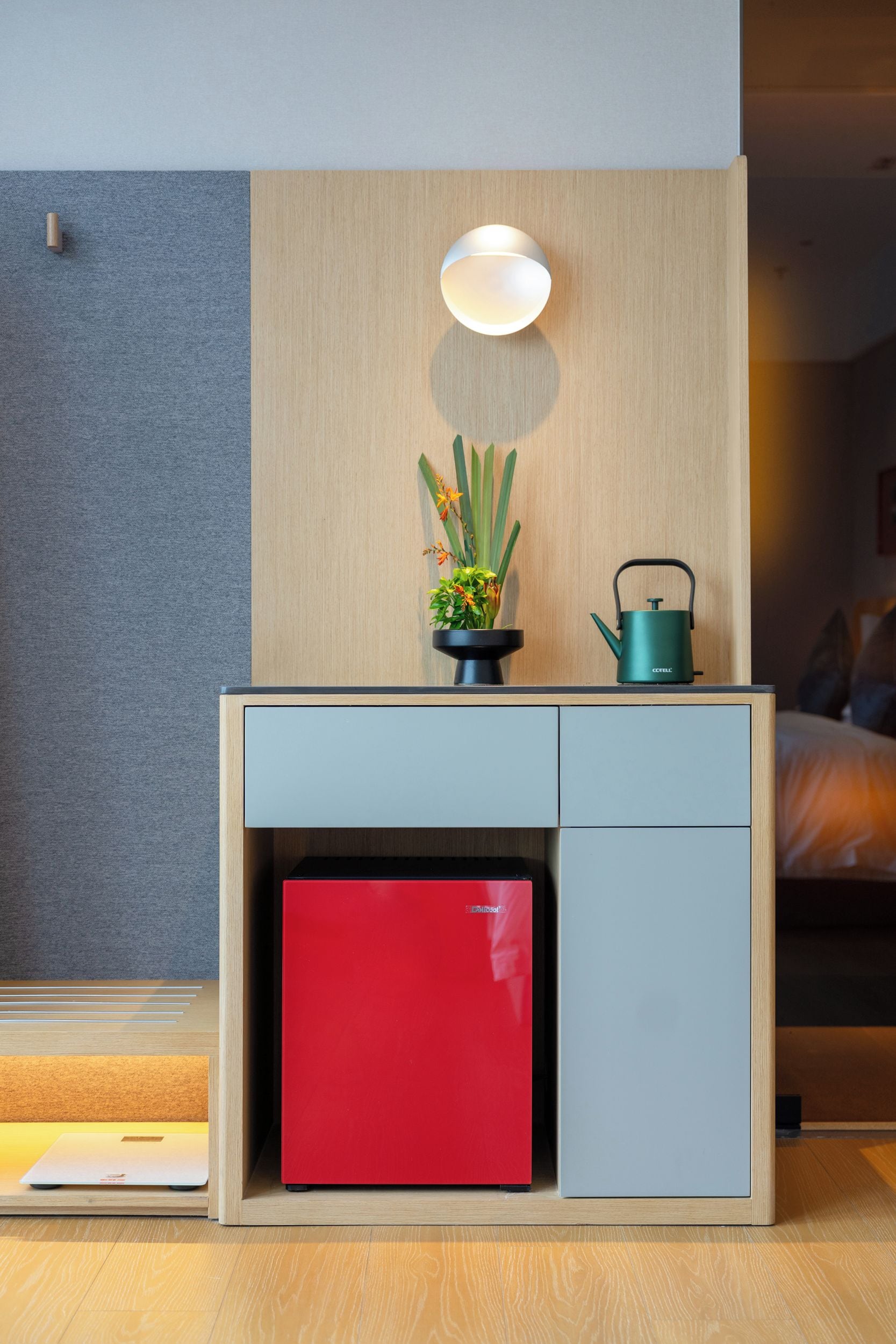 A compact, modern room with a wooden desk, a red cabinet, a potted plant, and a kettle.