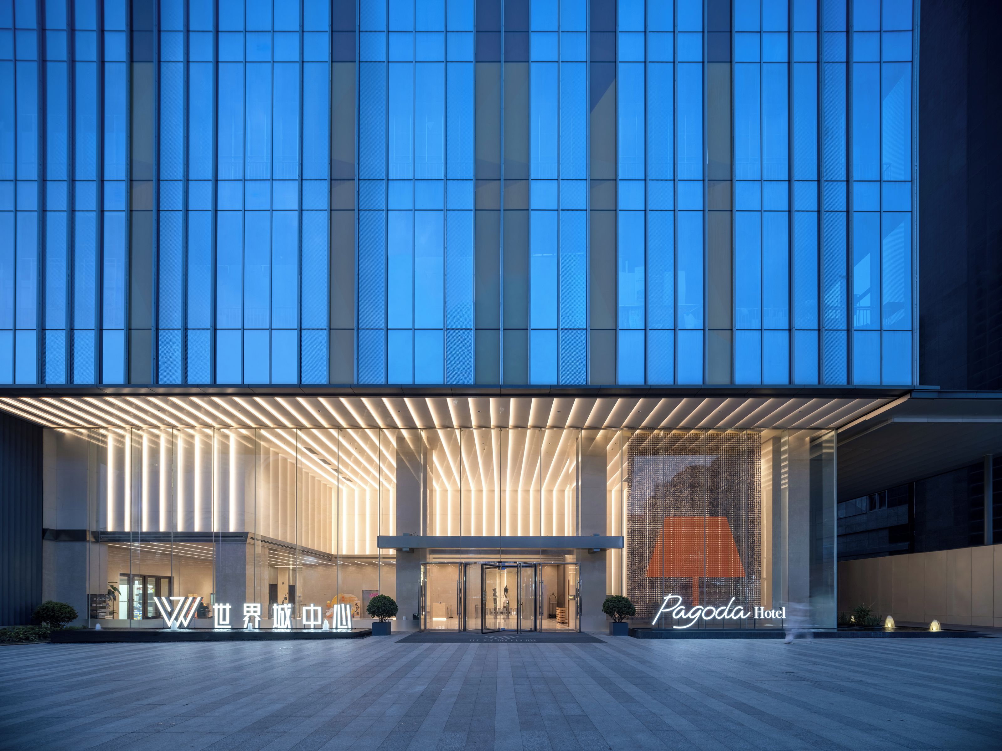 A modern hotel entrance with a glass facade, a prominent entrance canopy, and a neon sign for the hotel.