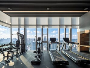 A gym with treadmills, dumbbells, and weight machines, large windows with a city view.