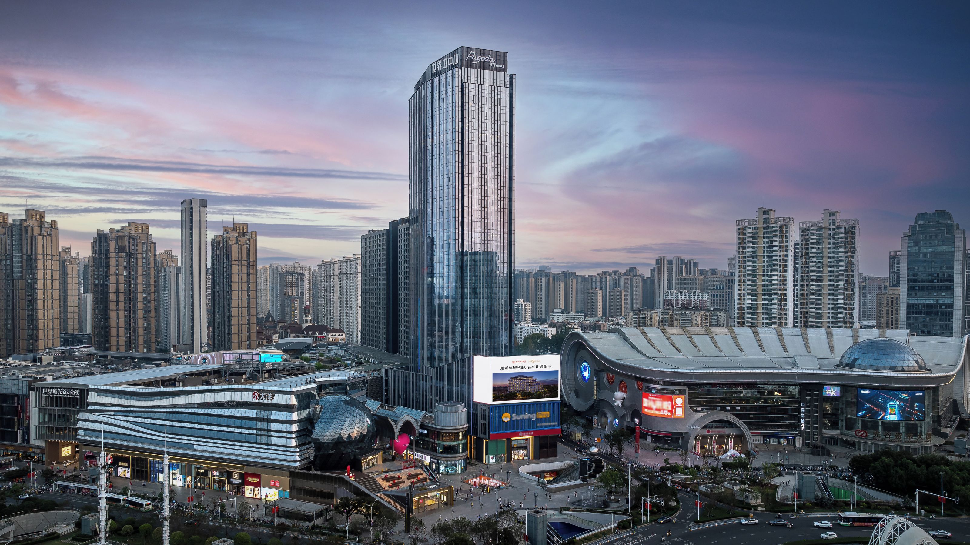 A cityscape with modern high-rise buildings, a distinctive curved building with a dome, and a large billboard.