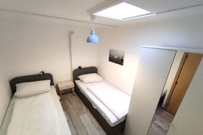 Ein kleines, kompaktes Zimmer mit zwei Einzelbetten, einem Schreibtisch, einem Stuhl und einem Dachfenster.