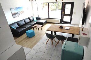 Ein modernes Wohnzimmer mit einem schwarzen Ledersofa, einem Holzesstisch mit Stühlen und einem großen Fenster.