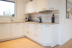 A modern kitchen with white cabinetry, a wooden countertop, and a window providing natural light. - Holiday home with 3 bedrooms (Timmendorfer Strand)