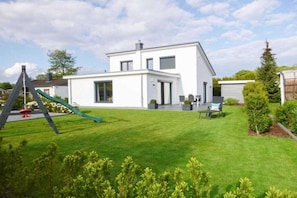 A modern two-story house with a well-maintained lawn and a swing set. - Holiday home with 3 bedrooms (Timmendorfer Strand)