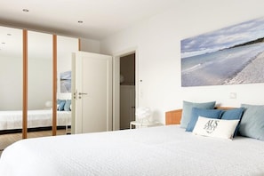 A bedroom with a bed, a wardrobe, a bedside table, and a wall-mounted picture of a beach. - Holiday home with 3 bedrooms (Timmendorfer Strand)