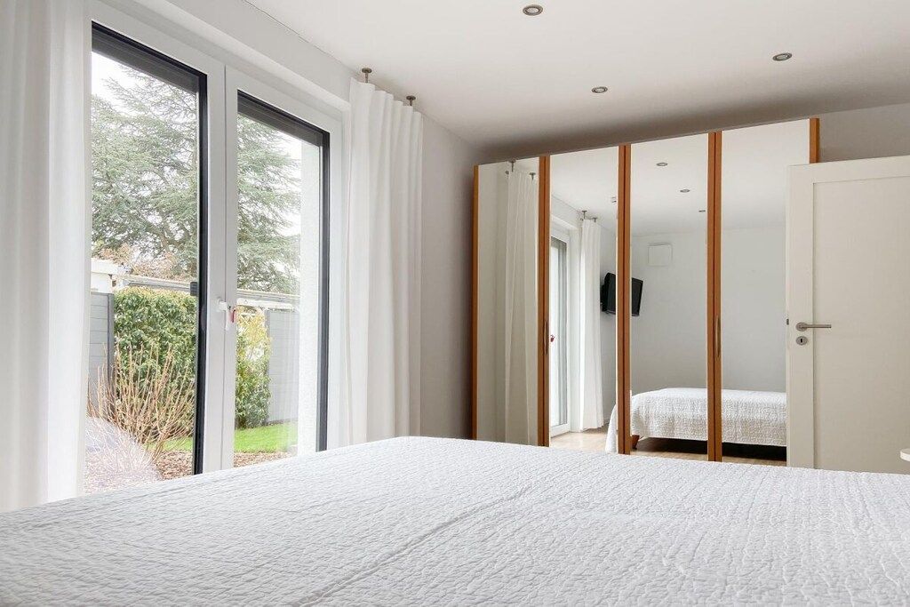 A bedroom with a large bed, sliding glass doors to a balcony, and a wardrobe with a mirror.