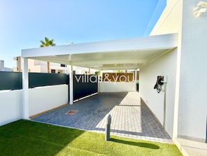 A covered outdoor area with a paved walkway, a grassy lawn, and a white wall. - Villa Soleada La Finca Golf by Villas&You (Algorfa)
