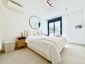 A modern bedroom with a large bed, a round mirror, a wardrobe, and a view of the outdoors. - Villa Soleada La Finca Golf by Villas&You (Algorfa)