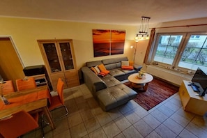 A living room with a sofa, dining table, chairs, a painting, and a window. - Beach butterfly Zingst (Zingst  (Fischland Darß))