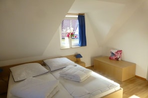 A bedroom with a bed, a bedside table, a lamp, a window with curtains, and a small bedside table with a flower vase. - Beach butterfly Zingst (Zingst  (Fischland Darß))