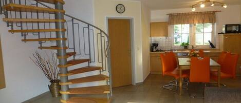A modern kitchen with a dining area, a spiral staircase, and a clock on the wall.