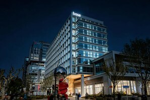 A modern building with the 'base' sign at the top, surrounded by trees and a reflective sculpture. - Base-CAOHEJING Hotel Residence (Shanghai)