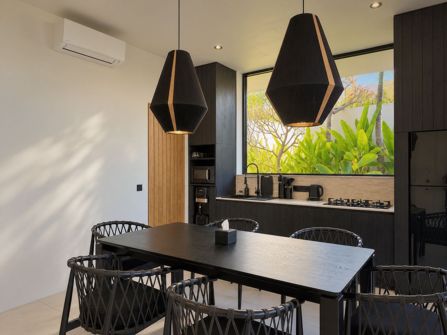 Eine moderne Küche mit großem Fenster, einem Essbereich mit dunklem Holztisch und Korbstühlen sowie Pendelleuchten mit geometrischem Design.