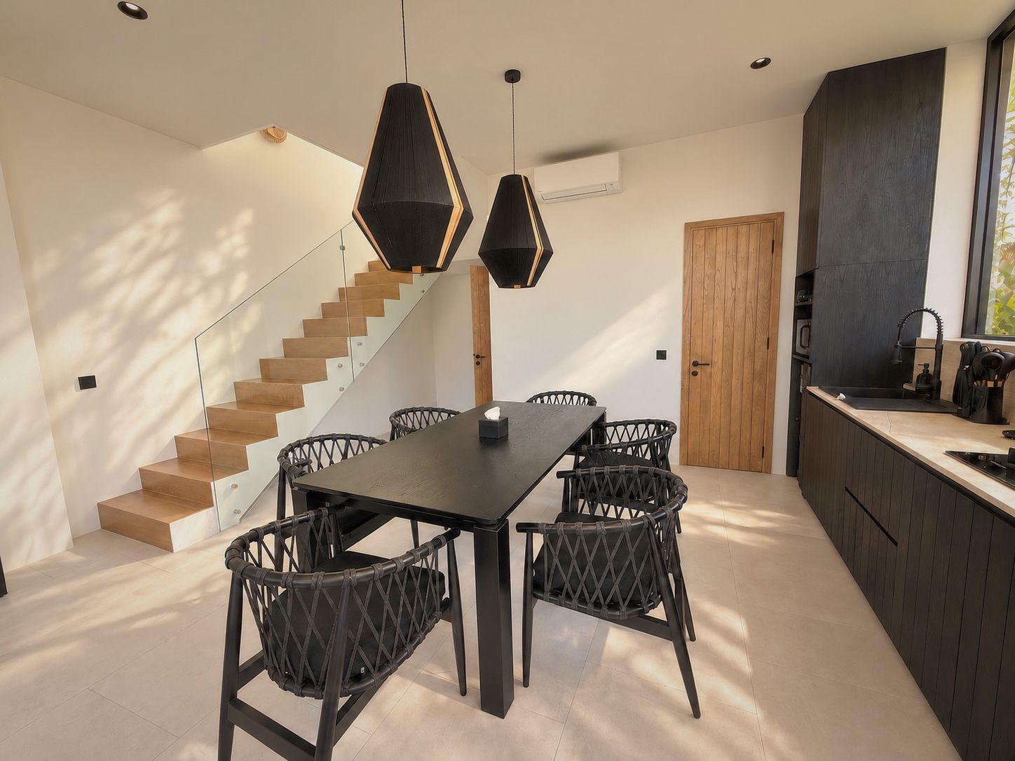 Eine moderne Küche mit dunklen Schränken, einer Holztreppe und einem Essbereich mit einem dunklen Tisch und Korbstühlen.