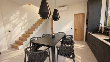 Eine moderne Küche mit dunklen Schränken, einer Holztreppe und einem Essbereich mit einem dunklen Tisch und Korbstühlen.