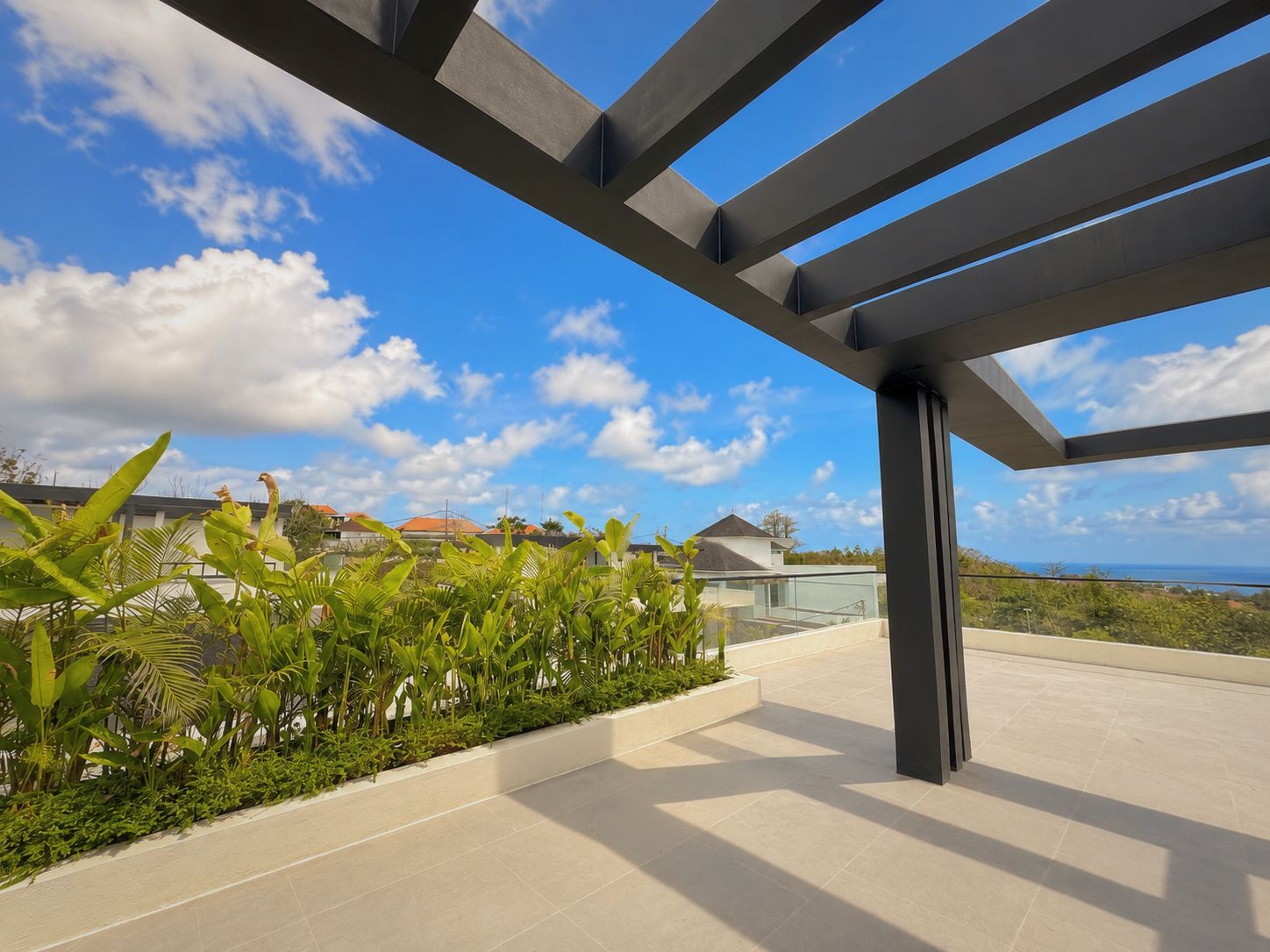 Eine moderne Terrasse im Freien mit freiem Blick auf den Ozean, umgeben von üppiger Vegetation und einer Pergola aus Metall.