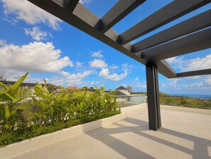 Une terrasse extérieure moderne offrant une vue dégagée sur l’océan, entourée d’une végétation luxuriante et agrémentée d’une structure de pergola en métal.